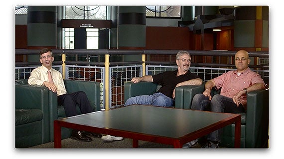 A trio of men sitting in chairs, discussing in a cozy indoor setting.