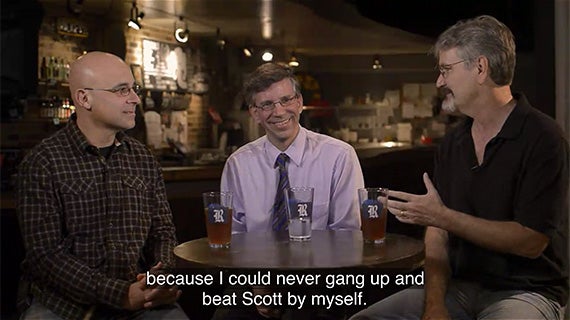 A table with three men sitting around it, each having a beer, sharing laughter and camaraderie in a relaxed setting.