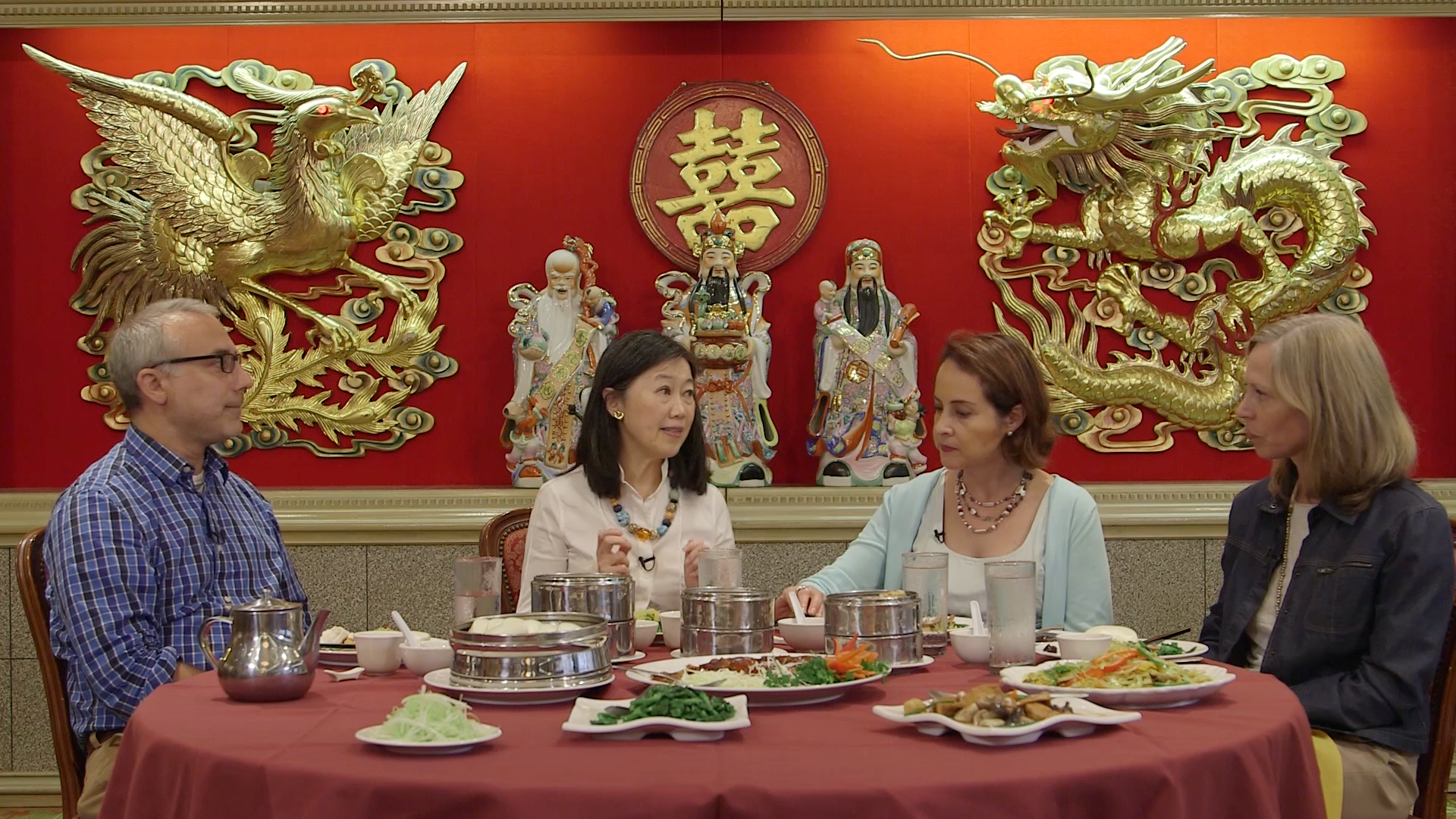 Several individuals seated at a table, sharing a meal with an assortment of food and drinks in a lively atmosphere.