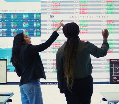 Two women engaged in discussion, pointing at a computer screen, highlighting important information together.
