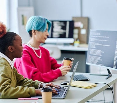 Two students working diligently on computers in an office environment, showcasing teamwork and productivity.