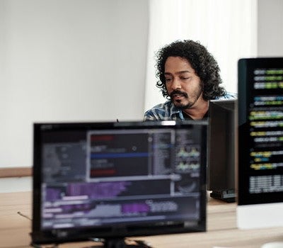A man working diligently at a desk, utilizing two monitors to enhance productivity and manage multiple tasks.