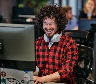 A smiling man with curly hair is focused on his computer, reflecting a positive and productive atmosphere.