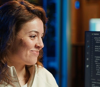A woman engaged in her tasks, seated at a computer, surrounded by a tidy workspace and natural light.